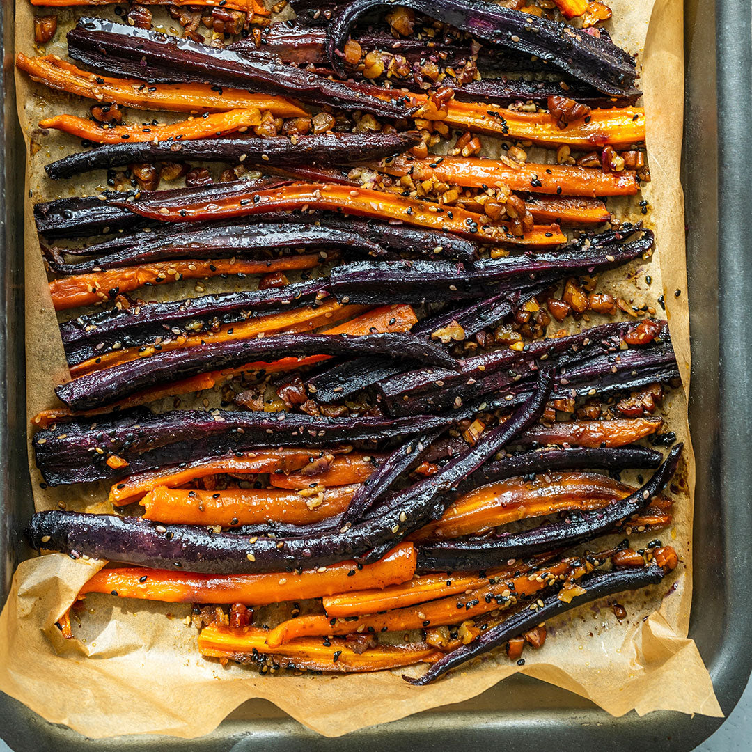 Roasted rainbow carrots seasoned with herbs and roasted garlic, arranged on a parchment-lined baking sheet.