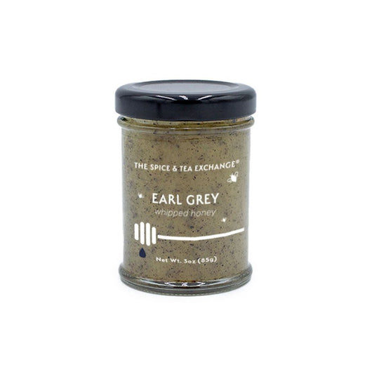 The Earl Grey Whipped Honey Jar from The Spice & Tea Exchange is a 3oz (85g) glass jar with a black lid, featuring creamy natural honey infused with Earl Grey flavor and a honey dipper illustration on the label.