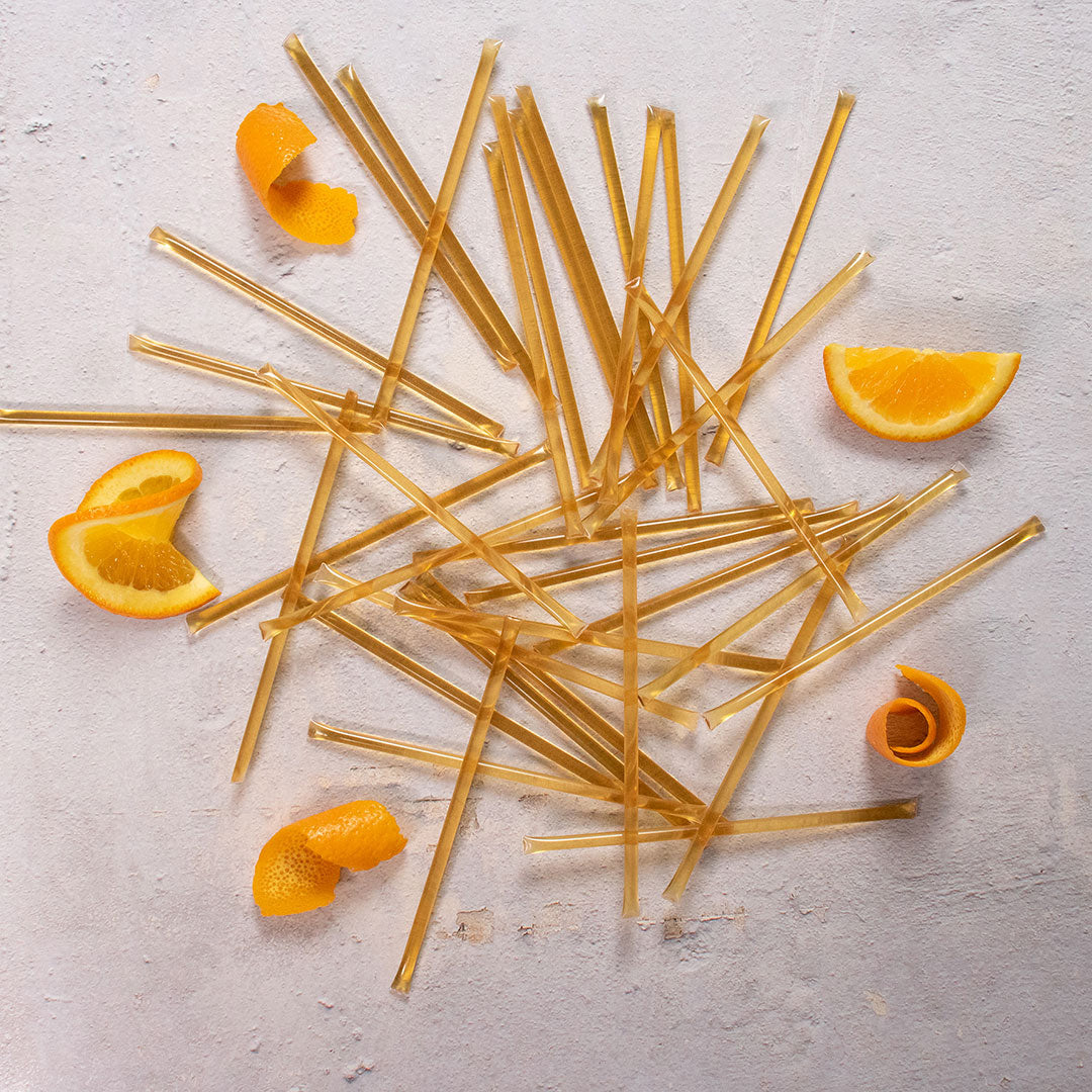 Orange Blossom Honey Straws are arranged across a light surface, surrounded by orange slices and orange peels.