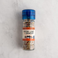 A clear glass spice and grinder bottle filled with a mixed spice blend, featuring a blue plastic cap and a white label with orange accents. The label reads 'Spice & Tea Exchange' and 'HOOK LINE & GRINDER SPICE BLEND'.