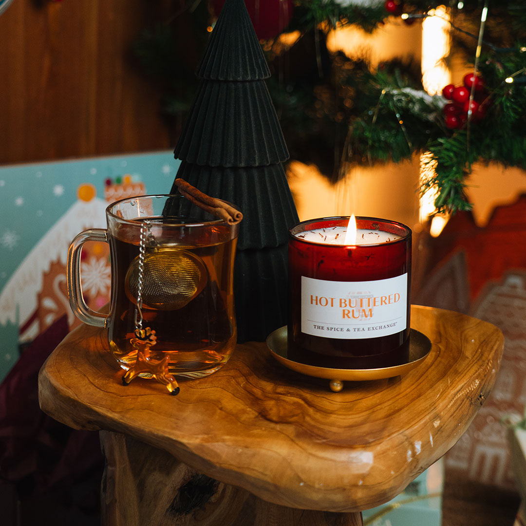 Hot buttered rum candle and glass mug on a wooden surface with festive background