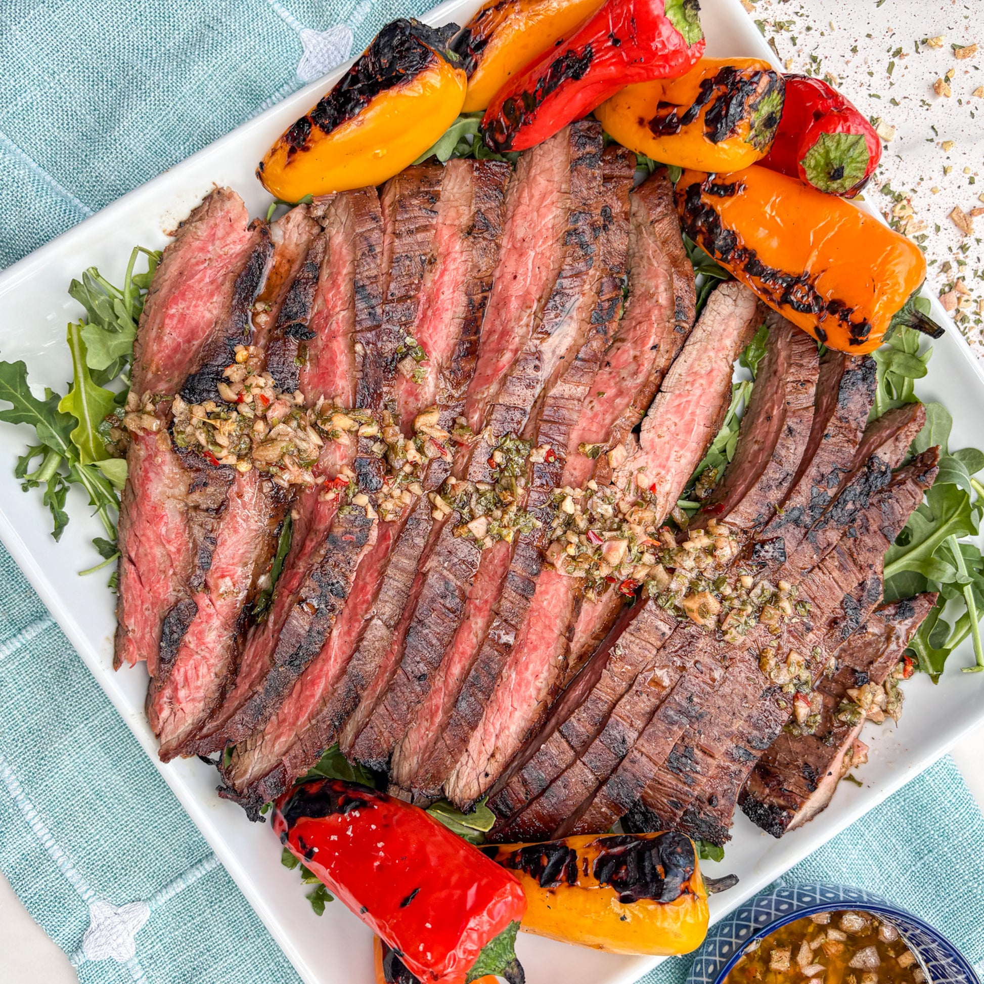 Grilled steak with grilled peppers on a white plate with a blue napkin.