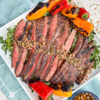 Grilled steak with grilled peppers on a white plate with a blue napkin.
