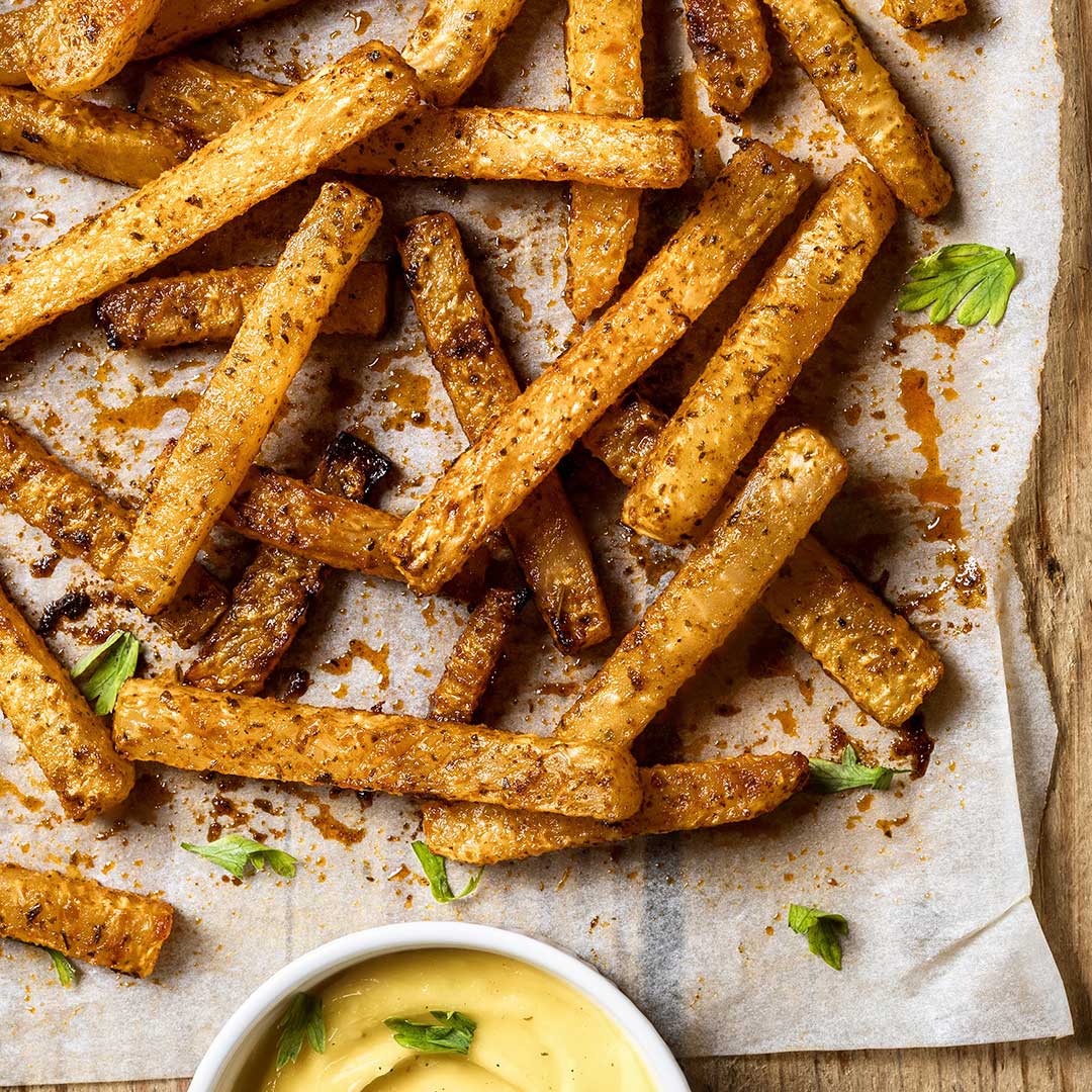 Crispy baked potato fries with a golden-brown seasoned coating, scattered on parchment paper with a small white dipping sauce bowl at the bottom.