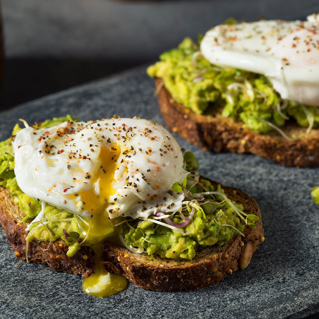 Poached eggs on top of avocado toast covered in guacamole and sprouts. Covered in seasoning.