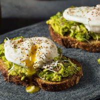 Poached eggs on top of avocado toast covered in guacamole and sprouts. Covered in seasoning.