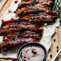 Grilled ribs on a wooden cutting board with a side of sauce.