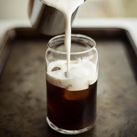 Cream poured into glass cup containing Iced Mocha Mushroom Herbal Tea