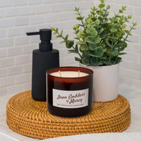 Candle with a label, black pump bottle, and green plant on a woven coaster.