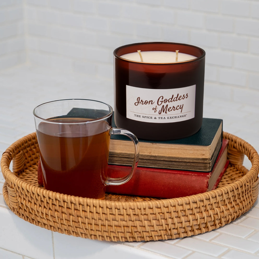 Candle labeled 'Iron Goddess of Mercy' with a mug of tea on a woven tray.