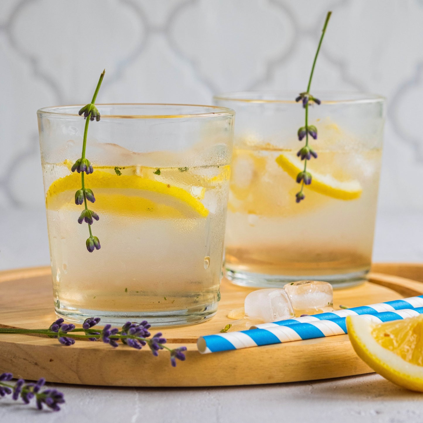 Two glasses of lemonade with lavender on a wooden tray.