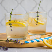Two glasses of lemonade with lavender on a wooden tray.