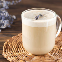Glass mug of creamy beverage with lavender flowers on a wooden surface