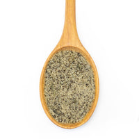 A wooden spoon filled with a coarse, granular green herb or spice blend, photographed from directly above on a plain white background.