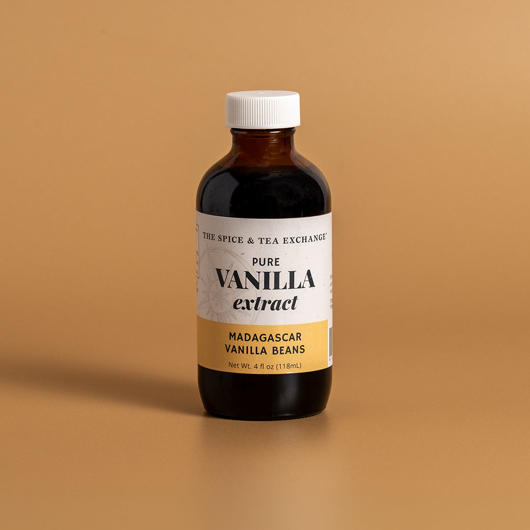 A bottle of Madagascar Vanilla Extract from The Spice & Tea Exchange, featuring a white label with a gold bottom section and a white cap, set against a solid tan background.
