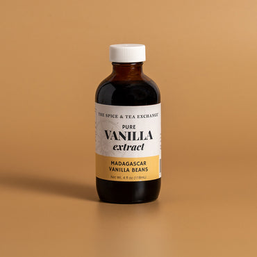 A bottle of Madagascar Vanilla Extract from The Spice & Tea Exchange, featuring a white label with a gold bottom section and a white cap, set against a solid tan background.