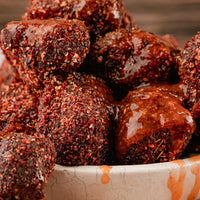 Close-up of glazed, spice-coated burnt rib end pieces piled in a white bowl with a rustic wooden background.