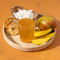 Mango Tango Herbal Tea in glass mug next to mango slices, dried pineapple slices, and coconut shreds