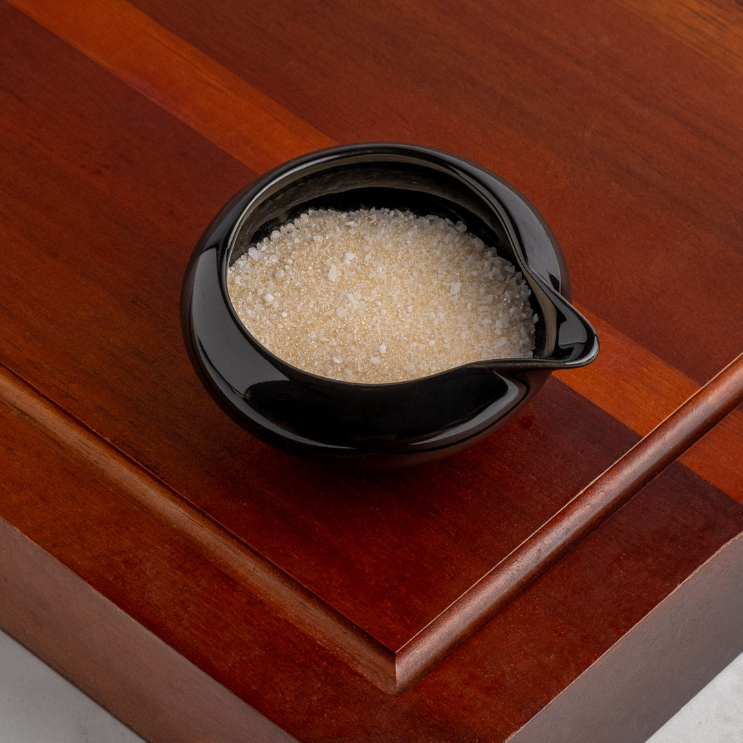 Black ceramic sugar bowl filled with sugar on a wooden surface