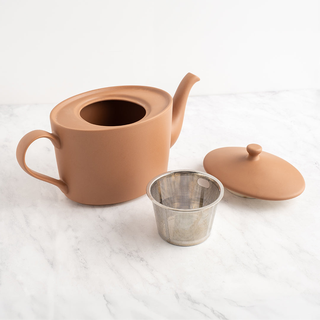 Ceramic mocha mousse teapot with a metal tea infuser on a white surface