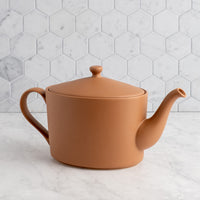 Mocha mousse teapot on a marble surface with a hexagonal tile backsplash.