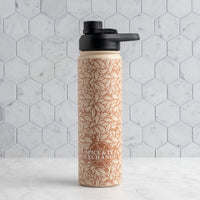 A reusable water bottle with a black flip-top lid, featuring a warm beige botanical leaf pattern and the 'Spice & Tea Exchange' logo, set against a light gray hexagonal tile background.