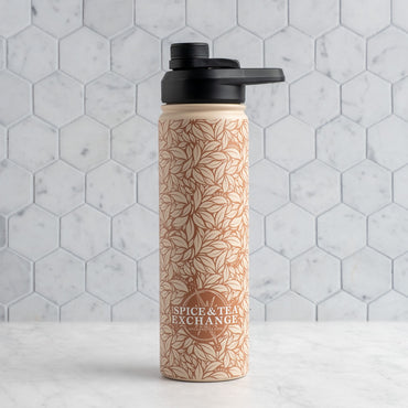 A reusable water bottle with a black flip-top lid, featuring a warm beige botanical leaf pattern and the 'Spice & Tea Exchange' logo, set against a light gray hexagonal tile background.