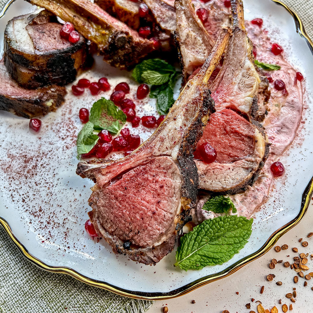 Moroccan Lamb Chops with pomegranate, mint leaves, on a white plate with gold trim.