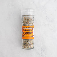 A clear plastic shaker bottle of Spice & Tea Exchange Orange Fennel Sea Salt, showing the salt inside, set against a light gray marble background.