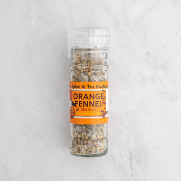 A clear plastic shaker bottle of Spice & Tea Exchange Orange Fennel Sea Salt, showing the salt inside, set against a light gray marble background.