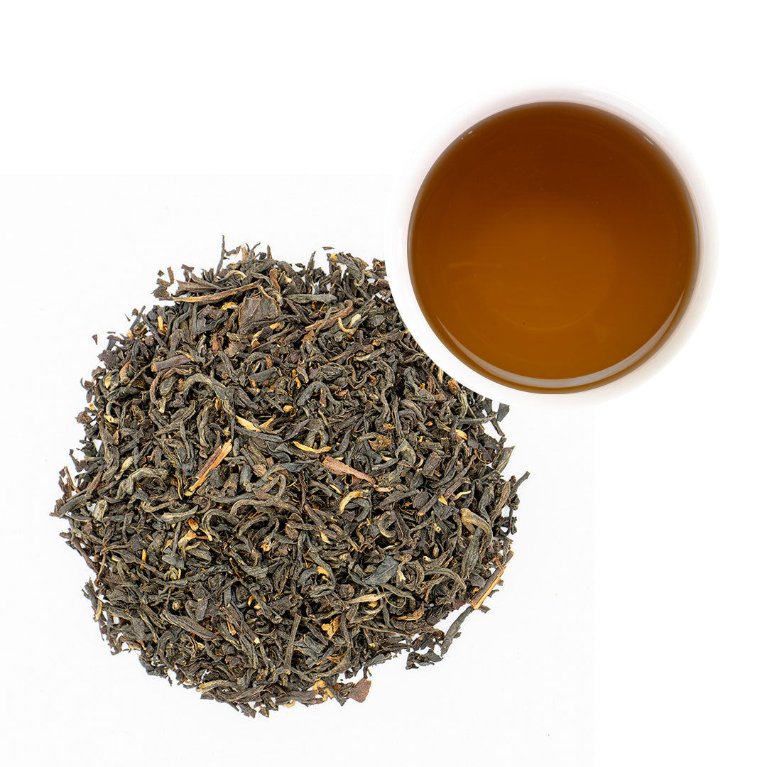 A pile of loose-leaf tea leaves next to a small cup of brewed amber tea on a plain white background.
