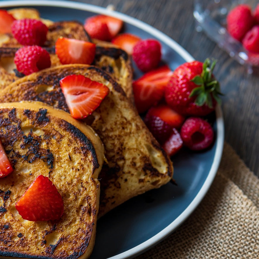 French toast slices on a dark blue plate, topped with fresh strawberries and served with additional berries on a rustic wooden table.