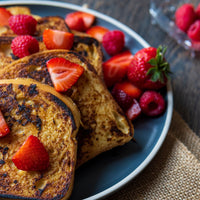 French toast slices on a dark blue plate, topped with fresh strawberries and served with additional berries on a rustic wooden table.