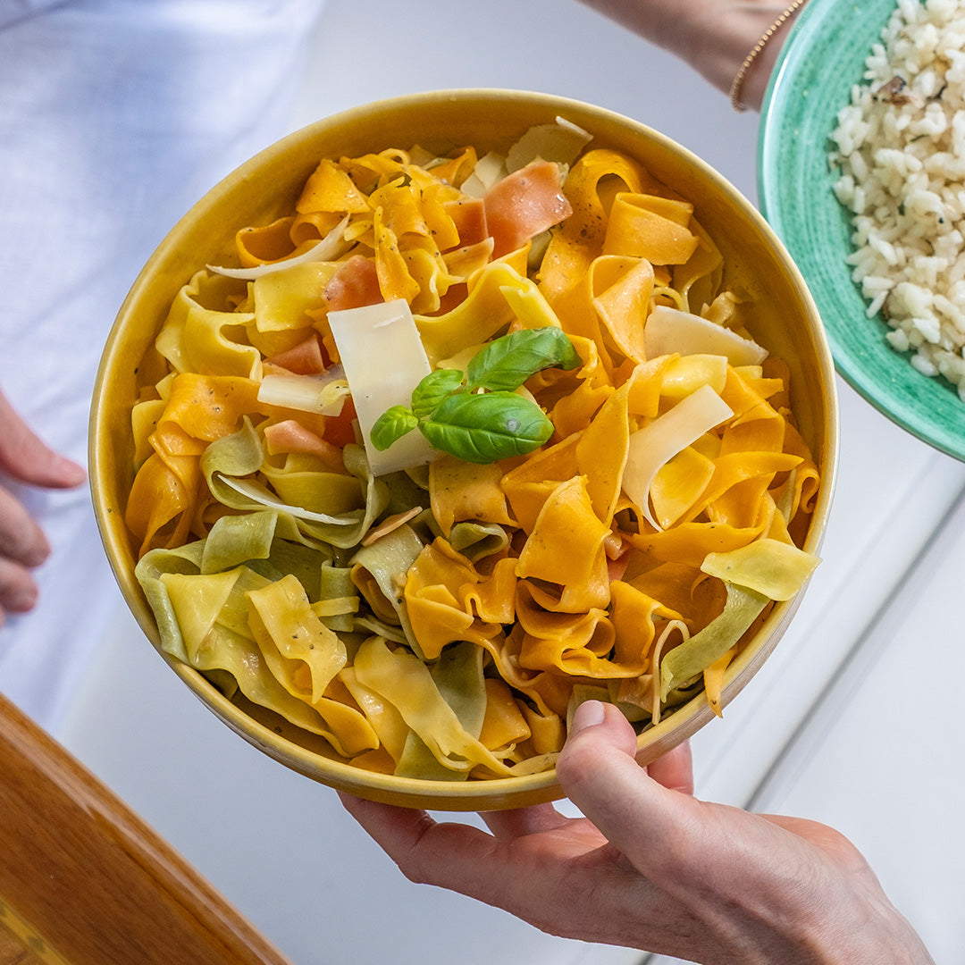 Yellow bowl filled with colorful pasta, held by a hand on a light background