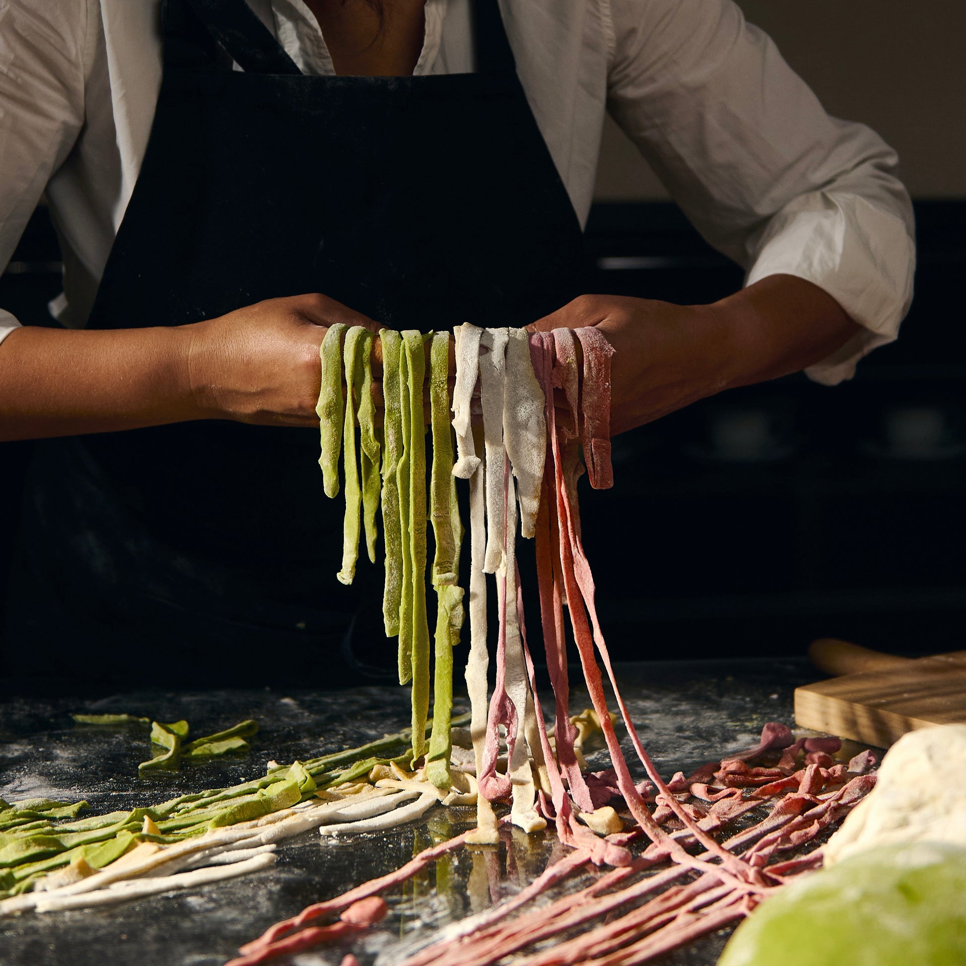 Person making fresh pasta with various colors on a dark surface.