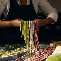 Person making fresh pasta with various colors on a dark surface.