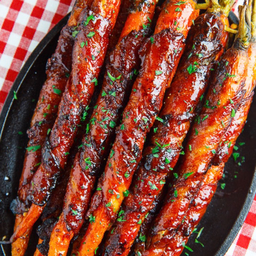 Grilled glazed carrots on a black serving platter, topped with chopped fresh parsley, set on a red and white checkered tablecloth.