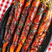 Grilled glazed carrots on a black serving platter, topped with chopped fresh parsley, set on a red and white checkered tablecloth.