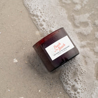 Candle labeled 'Peach on the Beach' on wet sand with foam