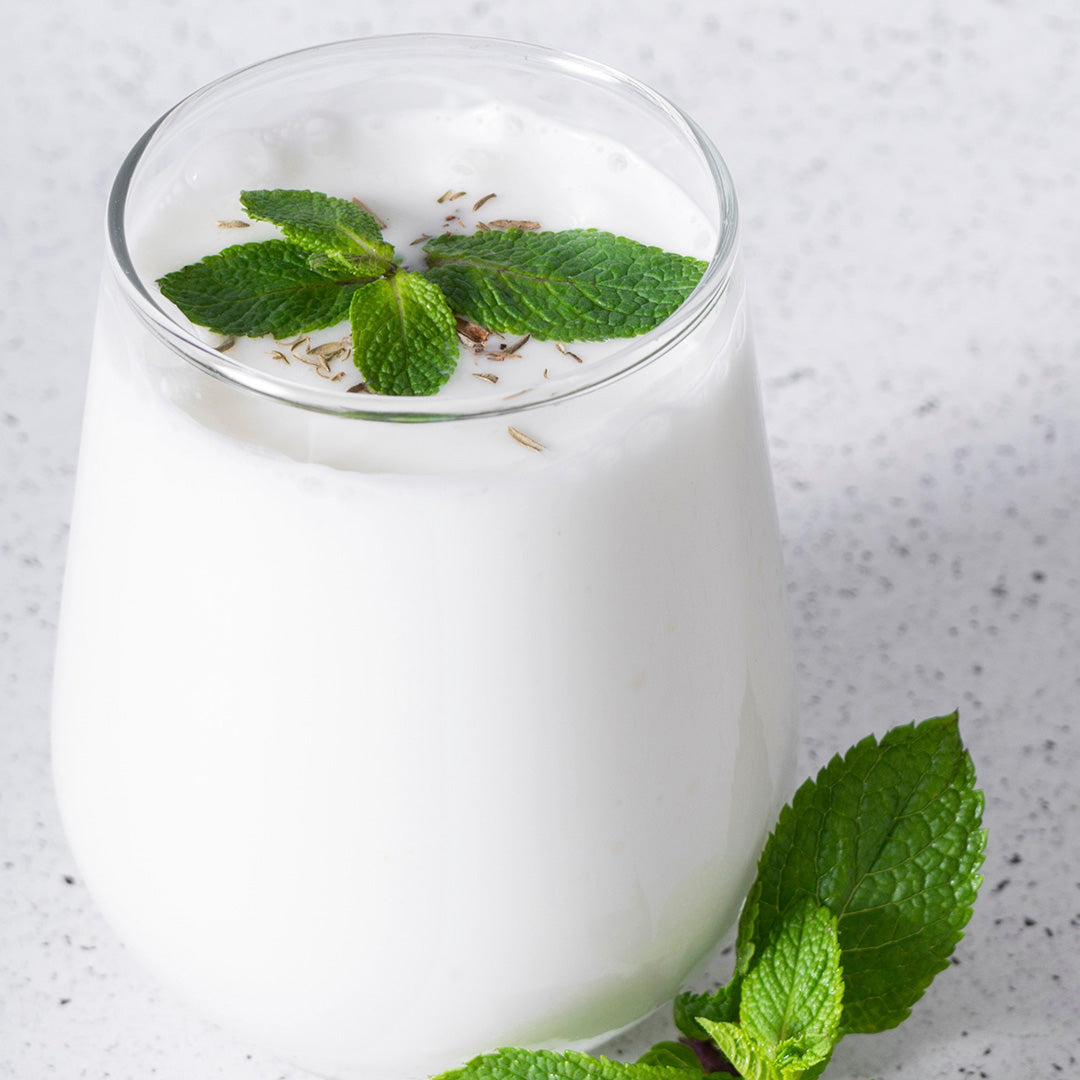 Glass of yogurt with mint leaves on a light gray background