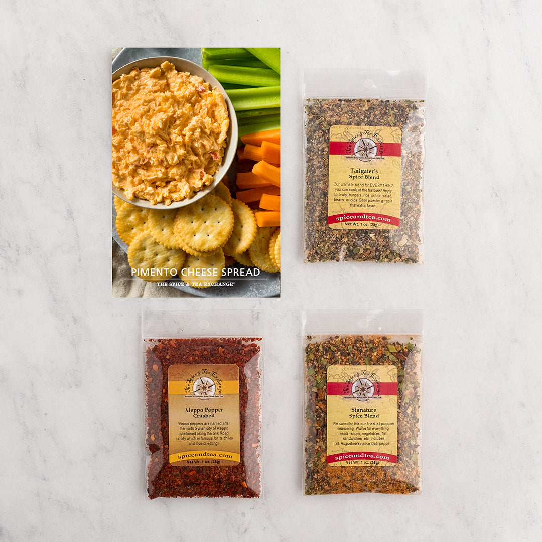 Three baggies of seasonings arranged on a white marble surface with a recipe card showing pimento cheese spread with crackers and celery.