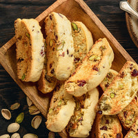 Biscotti cookies filled with pistachios and cranberries, arranged on a wooden serving tray with a few pistachios scattered on a dark wooden table.