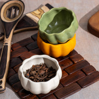 Three ceramic pumpkin bowls in green, orange, and white, on brown background.