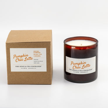 A Pumpkin Châi Latte scented candle in an amber glass jar next to its brown kraft cardboard box, both featuring white labels with orange text, on a clean white background.