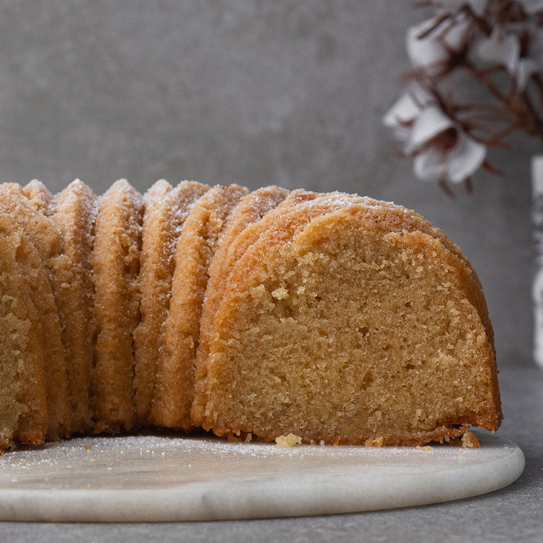 A sliced loaf of golden-brown cake on a round marble serving board against a textured gray background.