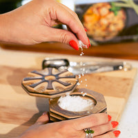 Person sprinkling salt from a Rainbow Pakkawood Salt Cellar on a cutting board.