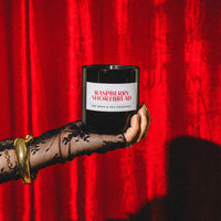 Hand holding a raspberry shortbread candle against a red curtain background