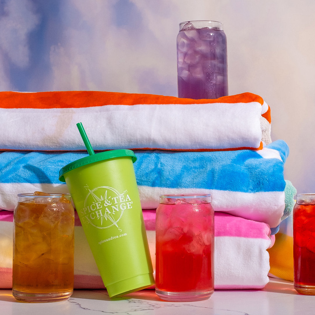 Green iced tea cup next to colorful glasses of iced tea and beach towels