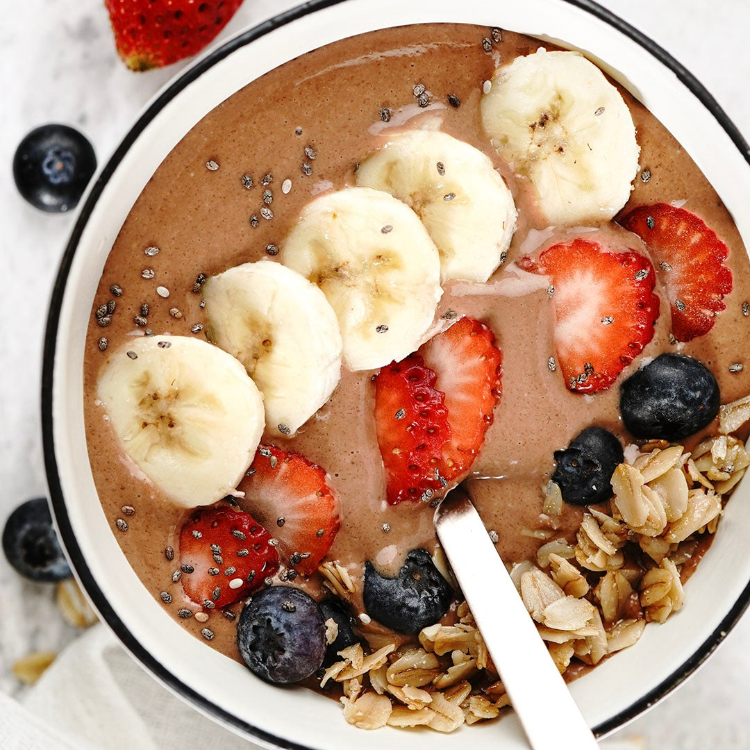 Chocolate smoothie bowl with bananas, strawberries, and blueberries in a white bowl.