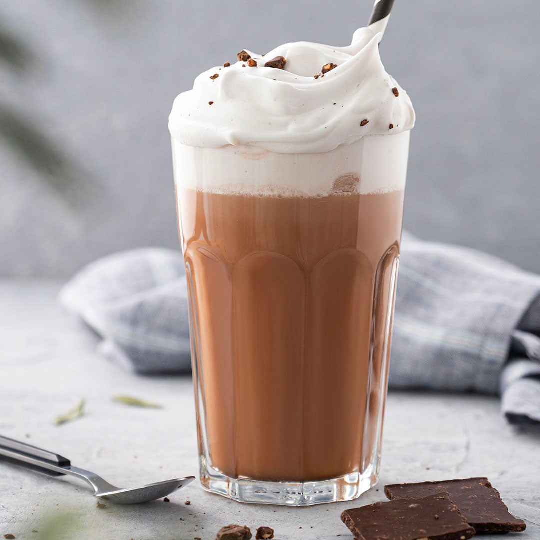 Glass of hot chocolate with whipped cream on a light surface